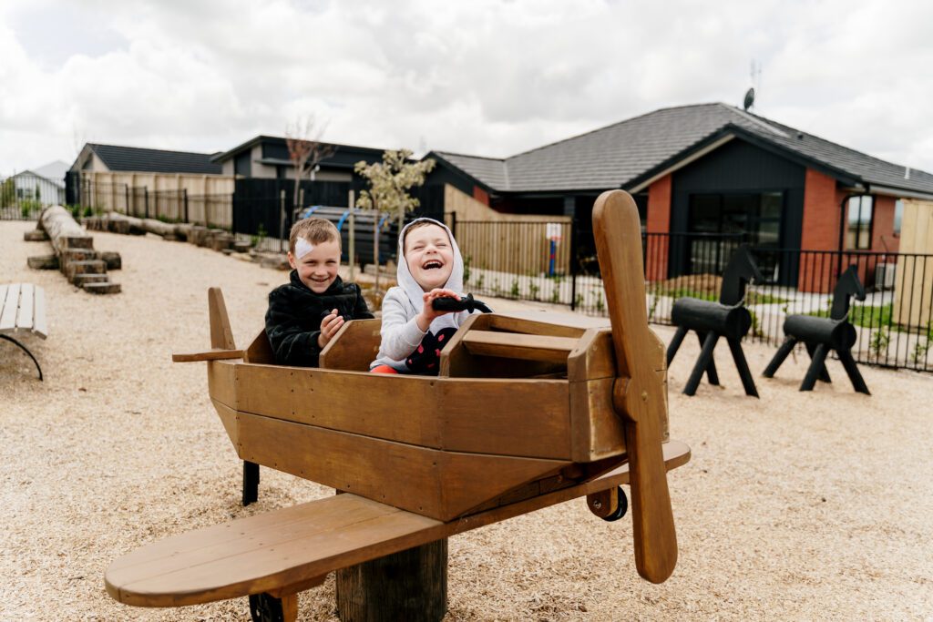 A very happy boys riding a wooden toy plane at Paerata Rise park