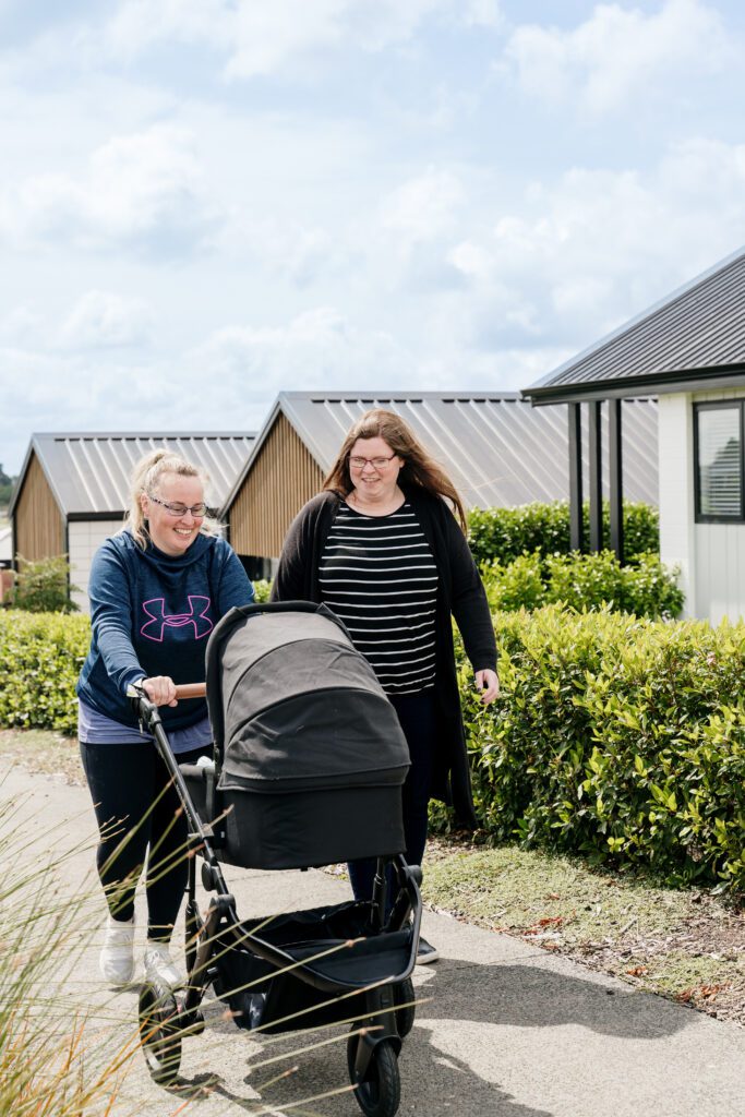 Two mothers walking with a baby where new houses have been build at Paerata Rise